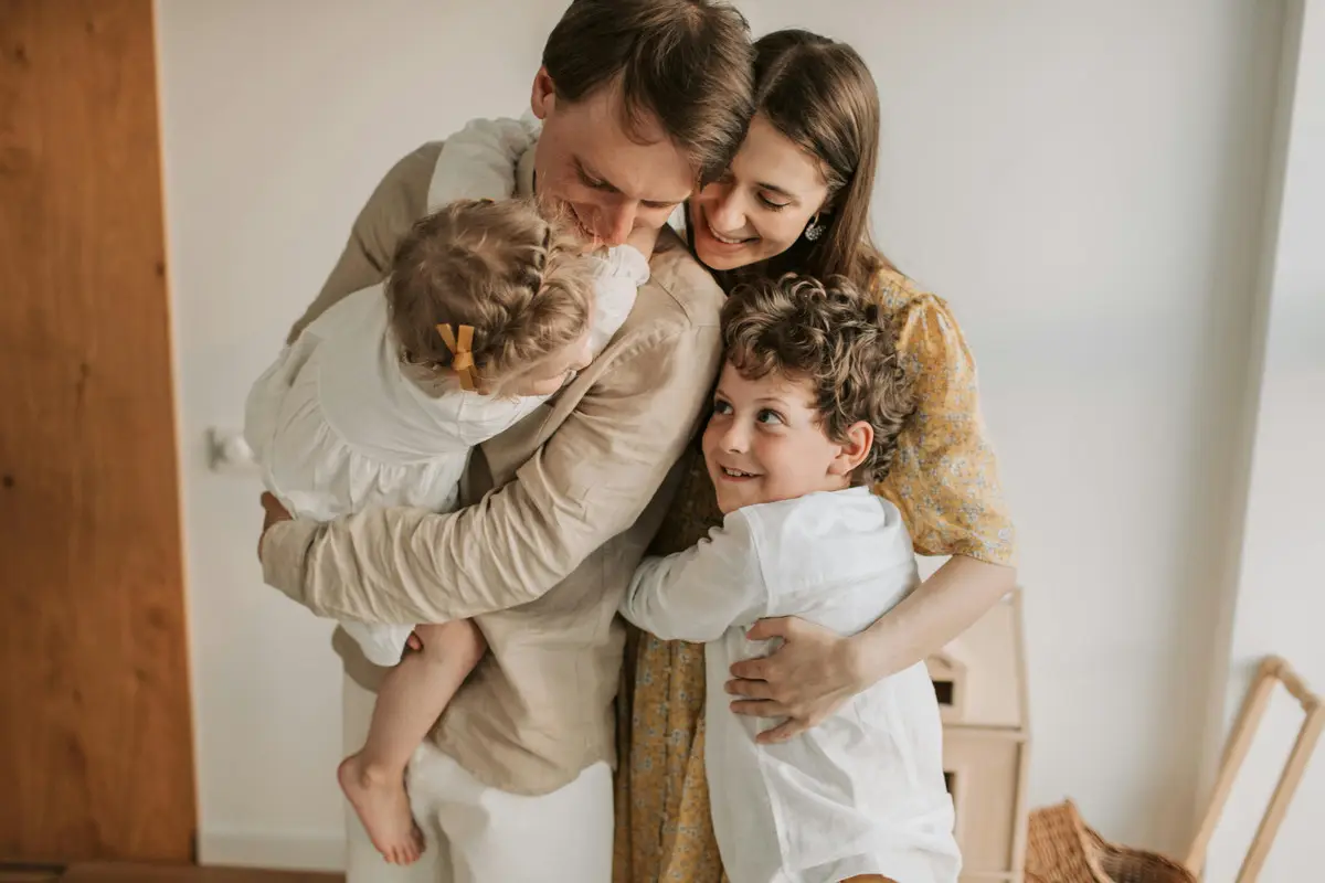Una famiglia si abbraccia in casa: i genitori tengono in braccio i due figli